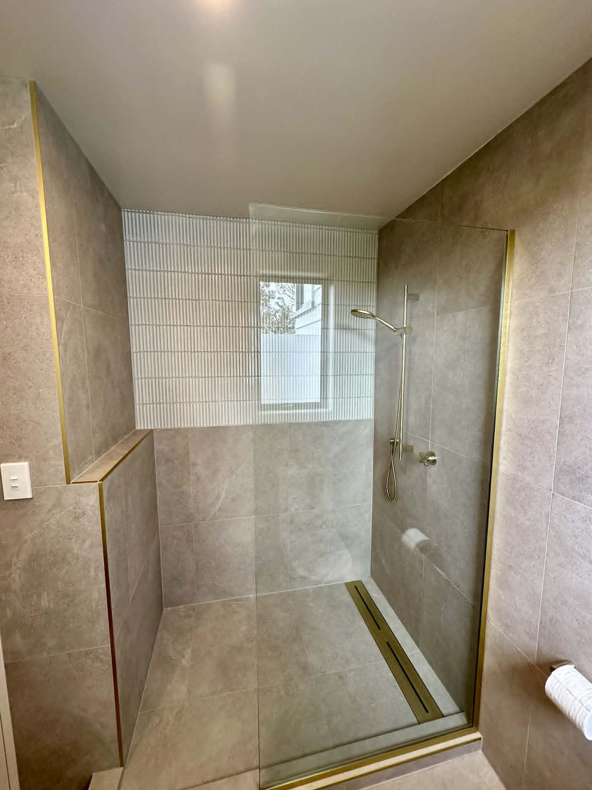St Heliers bathroom with warm stone tile, fluted feature wall and brass fittings